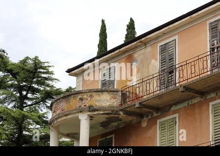 Abgerundeter Betonbalkon, der von zwei weißen Säulen neben einem länglichen Balkon mit verrosteten Metallzaun an der Seite eines alten verfallenen verlassenen Zimmers getragen wird Stockfoto