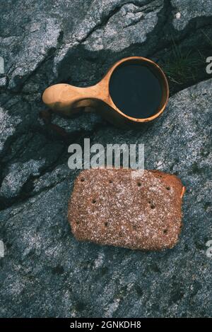 Finnische Guksi, gefüllt mit Kaffee, und ein Roggenbrot-Sandwich auf einem Felsbrocken an einem bewölkten und regnerischen Tag Stockfoto