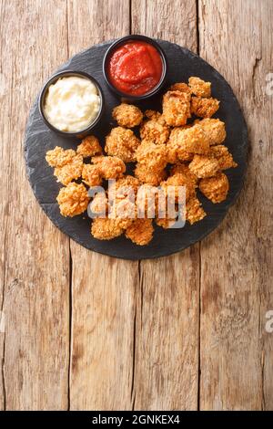 Popcorn-Huhn ist ein Gericht, das aus kleinen, mundgroßen Hähnchenstücken besteht, die in der Schieferteller auf dem Tisch paniert und in der Nähe gebraten wurden. Ve Stockfoto