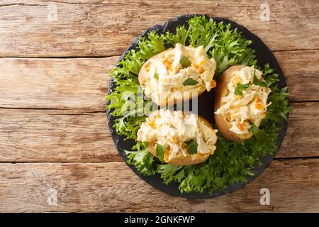 Englische gebackene Kartoffeln mit Krönungshuhnsalat aus der Nähe auf einem Schieferbrett auf dem Tisch gekrönt. Horizontale Ansicht von oben Stockfoto