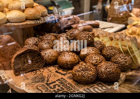 Frisches Gebäck in der Bäckerei. Schwarze runde Brötchen, mit Getreide bestreut. Frisches Gebäck, braune kleine Burger. Stockfoto