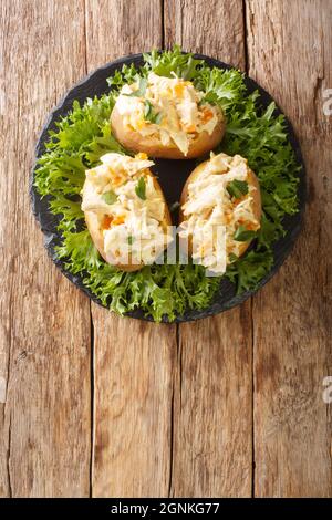 Gebackene Kartoffeln gefüllt mit Krönungshuhnsalat aus nächster Nähe auf einem Schieferbrett auf dem Tisch. Vertikale Draufsicht von oben Stockfoto