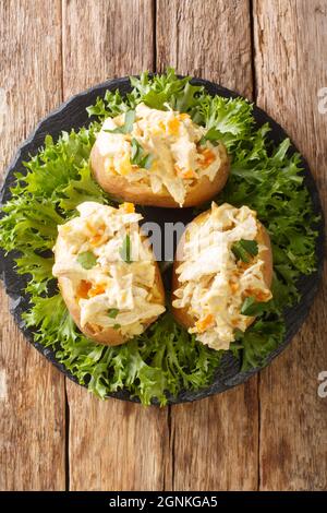 Coronation Chicken ist ein britischer Klassiker gekochtes kaltes Huhn in einer cremig-würzigen Sauce und gebackene Kartoffeln in der Nähe in der Schieferplatte auf dem Tisch. Vertica Stockfoto