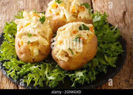 Hausgemachte heiße gebackene Kartoffeln gefüllt mit Krönungshuhnsalat aus der Nähe in der Schieferplatte auf dem Tisch. Horizontal Stockfoto