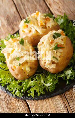 Coronation Chicken ist ein britischer Klassiker gekochtes kaltes Huhn in einer cremig-würzigen Sauce und gebackene Kartoffeln in der Nähe in der Schieferplatte auf dem Tisch. Vertica Stockfoto