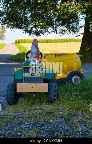 Ein Foto von Kindertraktor und gelbem Anhänger Parken auf dem Gras Stockfoto