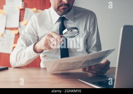 Geschäftsmann liest Vertragsdokumente mit Lupe am Schreibtisch, Nahaufnahme mit selektivem Fokus Stockfoto