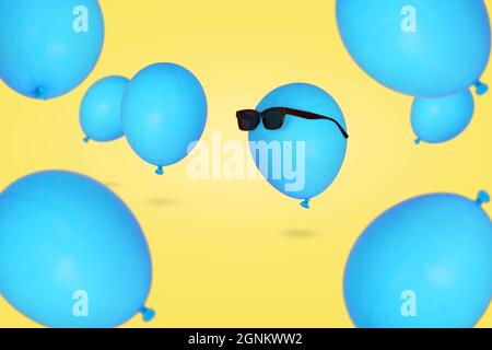 Blauer Ballon in Sonnenbrillen, der in der Luft schwimmt, mit anderen Ballons vor blauem Hintergrund. Minimales Konzept für Kreativität und Glück. Party-Stimmung, Stockfoto