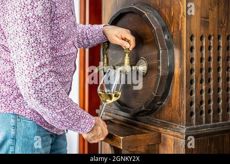 Person, die Wein aus einem Weinfass ausgießt. Reifer Sommelier im Keller des Weinguts gießt Rotwein in langstielige Weingläser. Stockfoto
