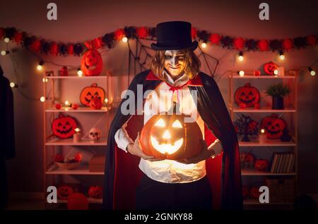 Erwachsener Mann in einem gruseligen Halloween-Kostüm, der seine lächelnde orangefarbene Jack-o-Laterne hält Stockfoto