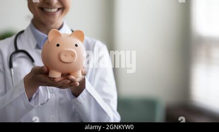 Lächelnde Hausärztin mit Sparschwein an den Händen Stockfoto