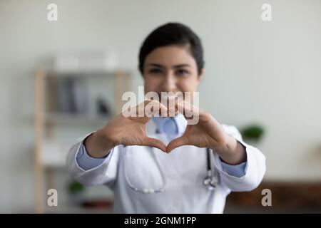 Glücklicher indischer Hausarzt, der die Herzform des Fingers bei der Kamera zeigt Stockfoto