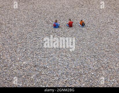 Drei Teenager sitzen an einem Kiesstrand in Wales Stockfoto