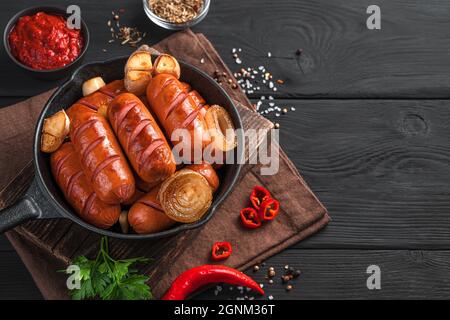 Leckere Würstchen mit Zwiebeln und Knoblauch in einer Pfanne auf dunklem Holzboden. Abendessen, Vorspeise mit Bier. Stockfoto