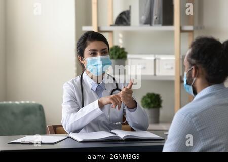 Junge indische Praktizierende in einer medizinischen Maske trifft sich mit dem Patienten Stockfoto