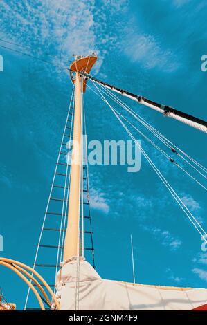 Seilrolle mit Seil auf einem klassischen Segelboot und einem Hintergrund aus blauem Wasser. Detailansicht des klassischen Mastes eines Segelbootes mit Seilrolle und Meer Stockfoto