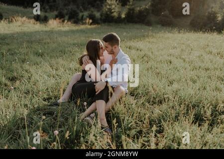 Ein junges Paar sitzt und posiert romantisch auf einer Wiese Stockfoto