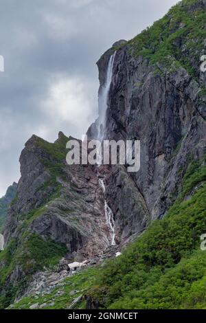 Felsiger Hügel mit Wasserfall, der in grünes Laub fällt - Gros Morne National Park - Western Brook Pond Stockfoto