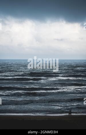 Ein Paar, das am leeren Strand entlang des stürmischen, dunkelsilbernen leuchtenden Ozeans in Daimus, Spanien, läuft Stockfoto