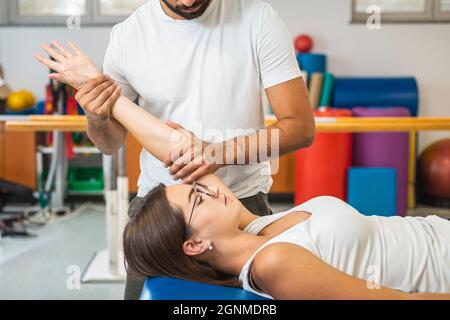 Männlicher Hysiotherapeut, der mit einer jungen Patientin in einer Klinik Übungen zur Ellenbogenverlängerung macht Stockfoto