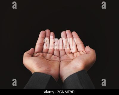 Junger Mann, der die Hände zum Gebet in der Luft hebt. Moderner Gebetsstil mit dunklem Hintergrund Stockfoto