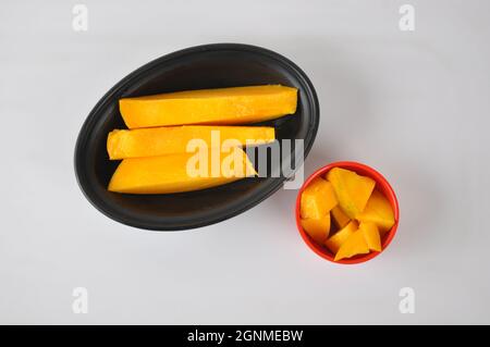 Die Mangoscheiben in der schwarzen Platte und eine kleine rote Schale isoliert auf weißem Hintergrund Stockfoto