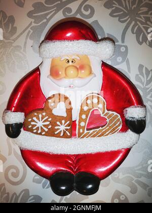 Kleiner Teller in Form des roten weihnachtsmannes mit Lebkuchenherzen, verziert mit weißer Glasur in Neujahrs- und Weihnachtsmustern Stockfoto