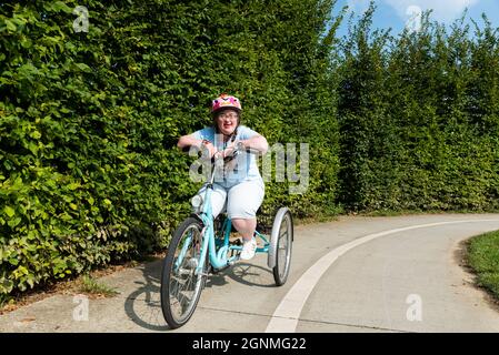 Hapendover, Flämisch-Brabant, Belgien - 09 20 2021: 39-jährige Frau mit Down-Syndrom auf der Straße mit ihrem Dreirad