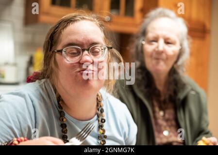 Die 39-jährige Frau mit Down-Syndrom und ihre 82-jährige Mutter mit Demenz essen zu Hause zusammen Stockfoto