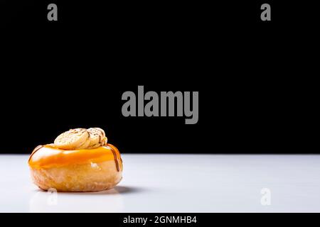 Foto eines cremigen Donuts mit Schokolade und Keksen auf einem weißen Tisch und schwarzem Hintergrund.das Foto wurde im horizontalen Format A aufgenommen Stockfoto