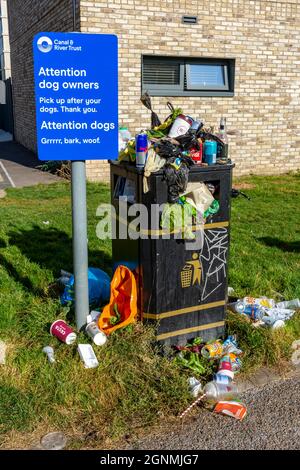 Schild, das Hundebesitzer bittet, neben einem gepackten und überlaufenen Abfalleimer nach ihren Hunden abzuholen. Am Ashton-Kanal, Ancoats, Manchester, England, Großbritannien Stockfoto