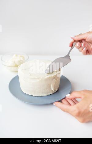 Köstliche cremige Torte, die das Mädchen mit einem Spatel über die Schlagsahne verteilt, ist der Kuchen bereit zur Dekoration Stockfoto