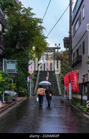 tokio, japan - 23 2020. november: Menschen, die an einem regnerischen Abend Regenschirm halten, gehen auf die Treppe des Yushima Tenmangu-Schreines in der Shiraaume-Einkaufsstraße Stockfoto