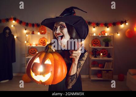 Glückliche Frau im Hexenkostüm, die Jack-o-Laterne hält und mit dem Finger auf dich schüttelt Stockfoto