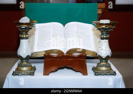 Die Heilige Bibel öffnet sich auf einem Holzaltar und einem Kerzenständer an der Seite Stockfoto