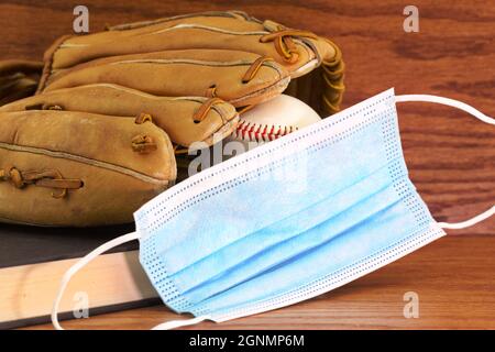 Konzept der Schulsportler und Covid-19-Schutzempfehlungen in getragenem Baseballspiel und Handschuh mit Büchern und medizinischer Maske auf Holz-Rückenplatte platziert gesehen Stockfoto