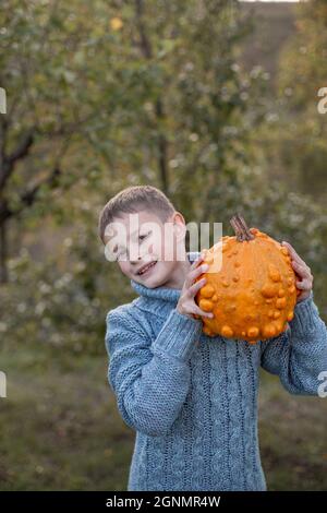 Deformierte hässliche orangefarbene Kürbisse in den Händen eines Kindes. Stockfoto