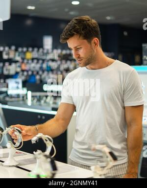 Junger männlicher Kunde untersucht moderne Smartwatch, während er elektronische Geräte im modernen Shop auswählt Stockfoto
