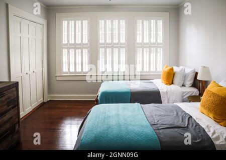Ein Gästezimmer mit zwei Einzelbetten mit türkisfarbenen und grauen Bettüberwürfen und gelben dekorativen Kissen Stockfoto