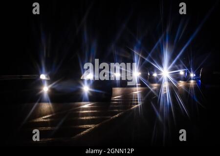 Im nächtlichen Stadtverkehr leuchtet das Auto im Regen, die Hauptverkehrszeit ist voll. Autoscheinwerfer durch die Regenscheibe verwandeln sich in bunte Lichtsterne Stockfoto