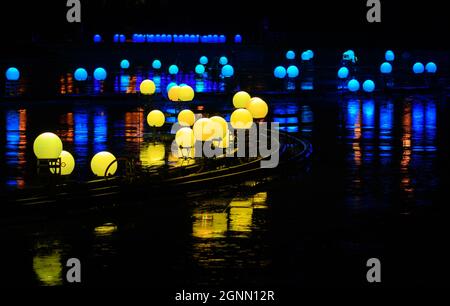 Ruhige Reflexionen im Wasser von bunten Nachtkugellampen im See des Stadtparks spät in der Nacht Stockfoto