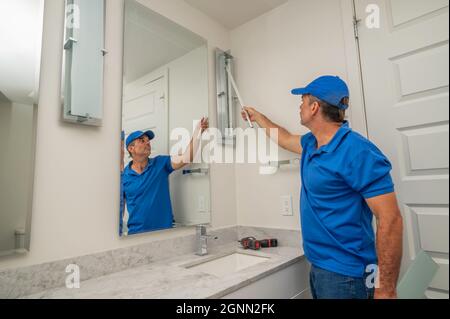 Handwerker vor einem Spiegel in einem modernen Badezimmer, der eine LED-Röhrenleuchte ersetzt Stockfoto