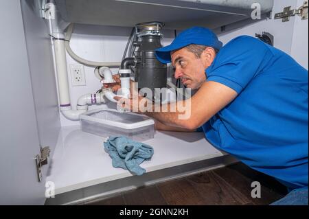 Professioneller Klempner, der an Rohren unter einem Spülbecken arbeitet Stockfoto