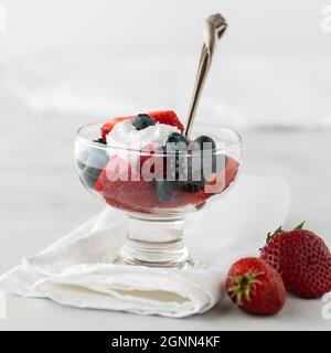 Ein Glas Dessertgericht gefüllt mit gemischten Beeren und gekrönt mit leichter Schlagsahne. Stockfoto