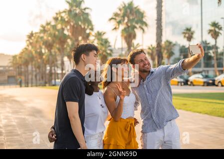 Gruppe fröhlicher junger multirassischer Freunde in legerer Kleidung, die Selfie auf dem Smartphone machen, während sie auf der Straße stehen und den Sommertag gemeinsam genießen Stockfoto