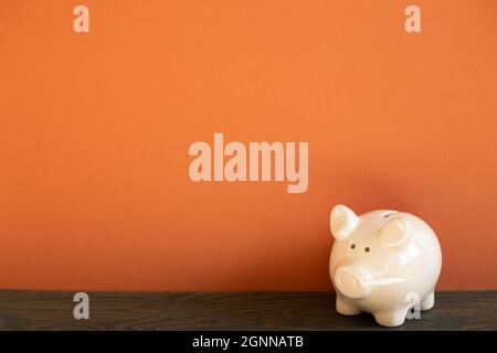 Rosa Sparschwein auf Holzschreibtisch. Roter Wandhintergrund Stockfoto