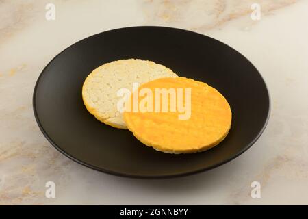 Zwei aufgeblasene Reiskuchen mit Apricot-Joghurt auf schwarzem Snackteller auf dem Tisch Stockfoto