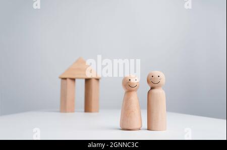Ein Paar beginnt ein Leben zusammen mit dem Immobilieninvestitionskonzept. Das fröhliche Menschenpaar aus Holz steht vor einem Holzhaus Stockfoto