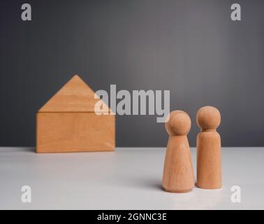 Ein Paar beginnt ein Leben zusammen mit dem Immobilieninvestitionskonzept. Das hölzerne Menschenpaar, das vor einer Holzhausminiatur steht Stockfoto