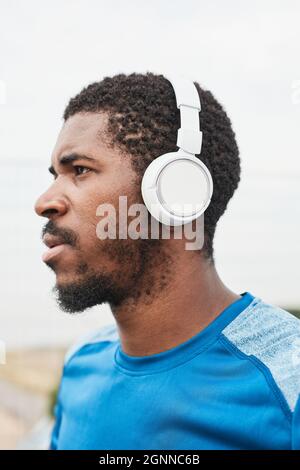 Afrikanischer junger Sportler mit kabellosen Kopfhörern, der im Freien Musik hört Stockfoto
